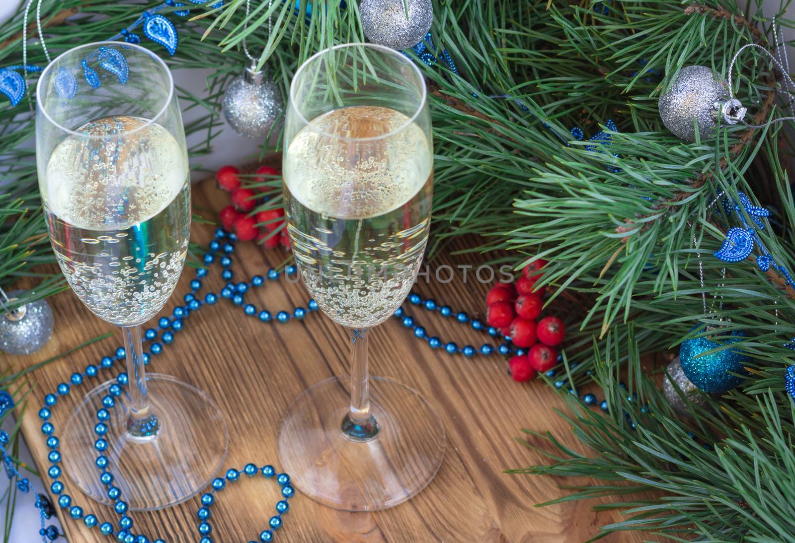 Christmas and New Year still life composition with two champaign glasses, pine tree acerose, red rowan berries, blue and silver balls, garland ornament decoration, copy space