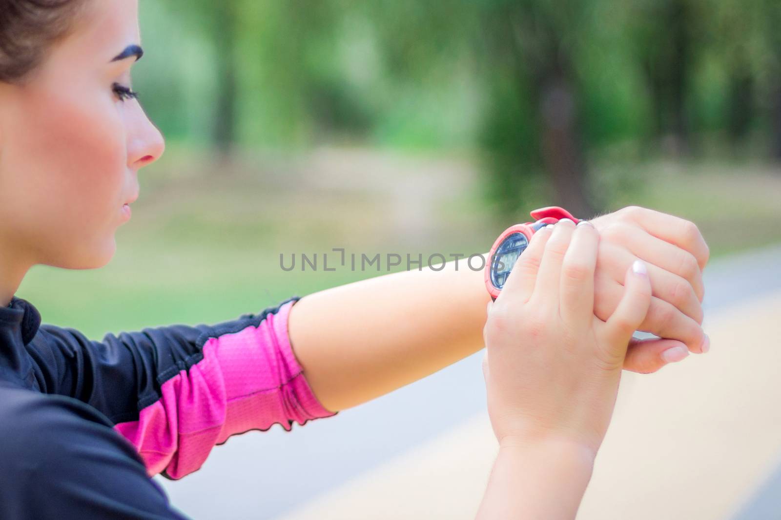 Young fitness girl checks stopwatch tracker on her wrist during running outdoor