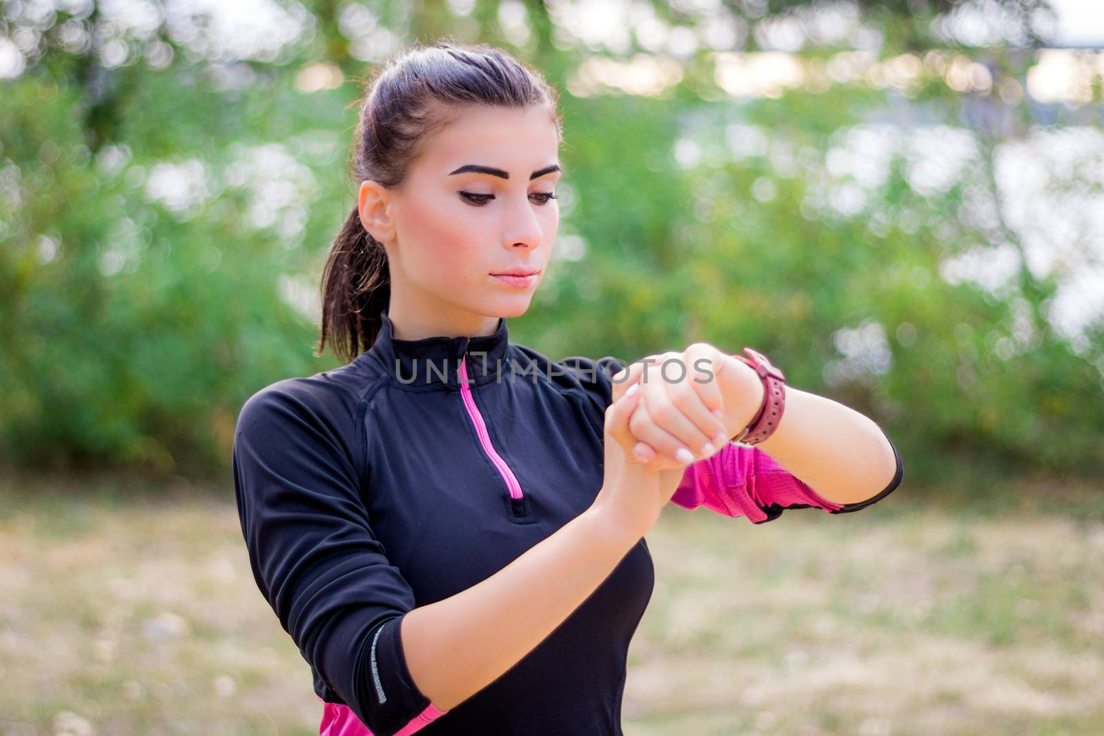 Young fitness girl checks stopwatch tracker on her wrist during running outdoor