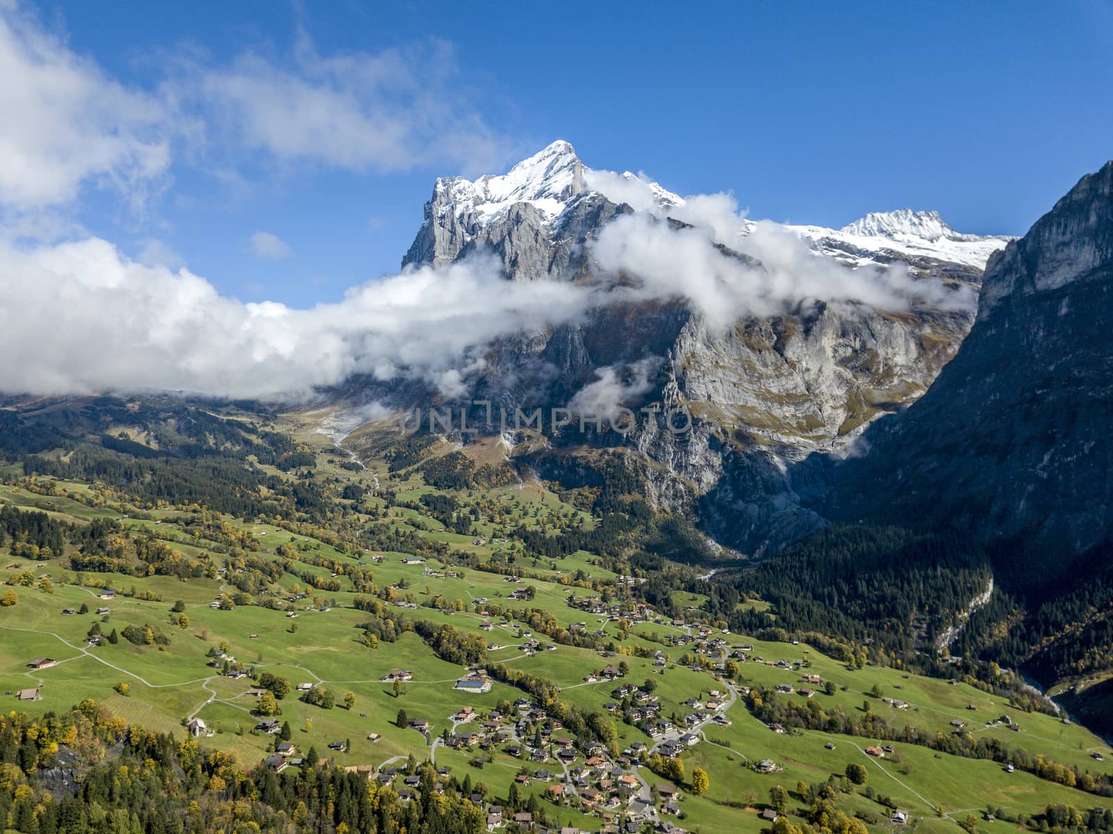 Amazing dream like Swiss alpine mountain landscape, wooden chalets on green fields and high mountains with snowy peaks background, in Grindelwald of Switzerland.