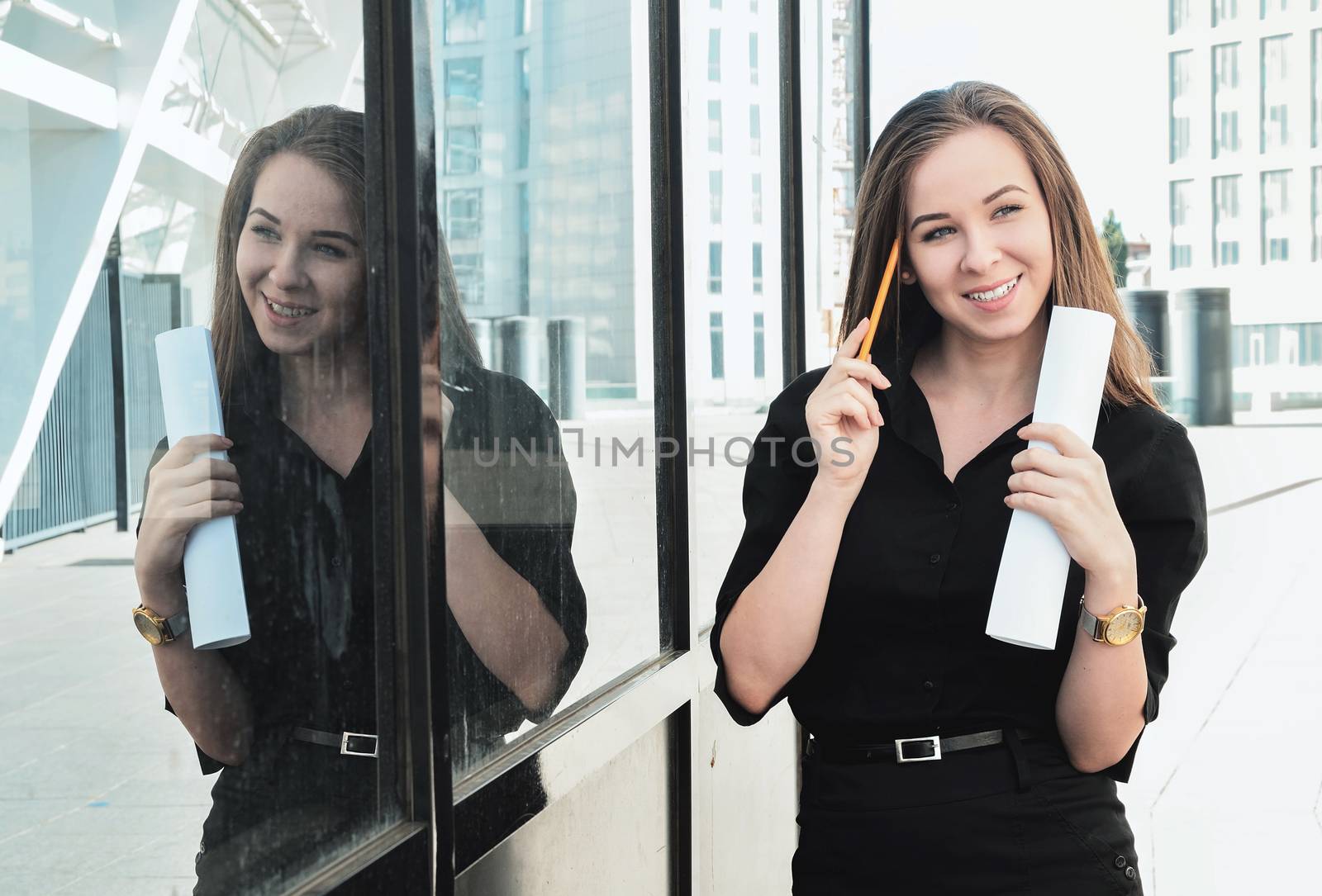 A beautiful young girl reflects on a complex technical project, standing outdoor near the building smiling, holding a pencil near her head