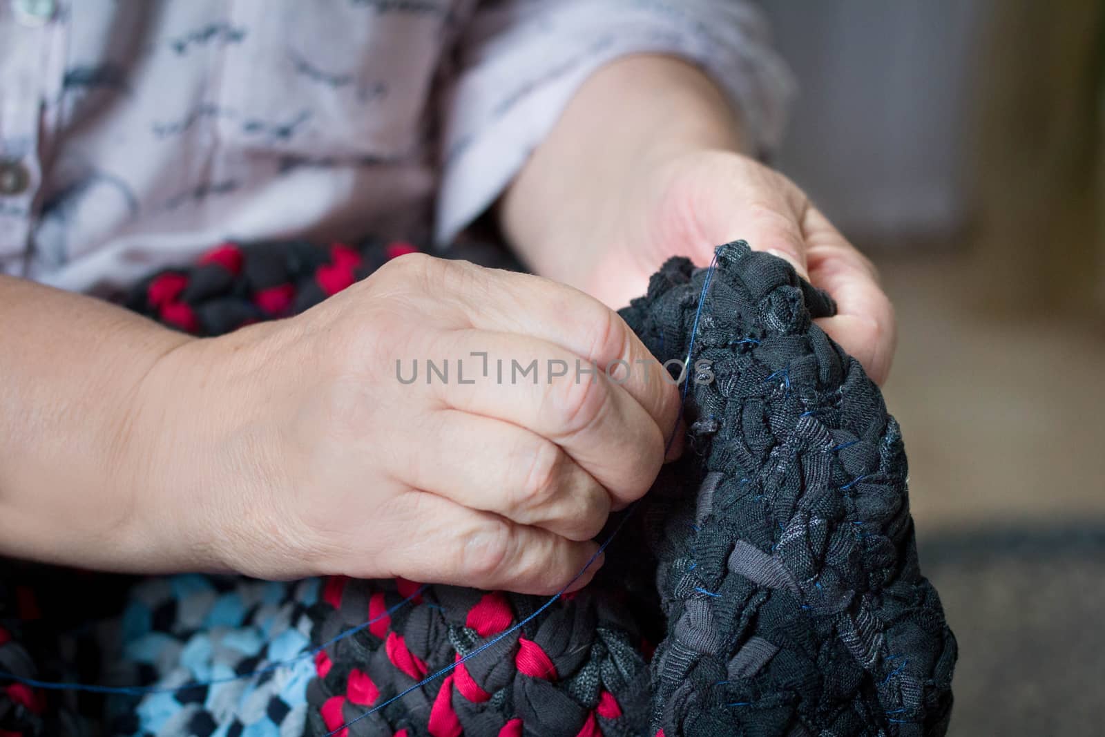 Elderly lady sews with needle and thread doing hand work by VeraVerano