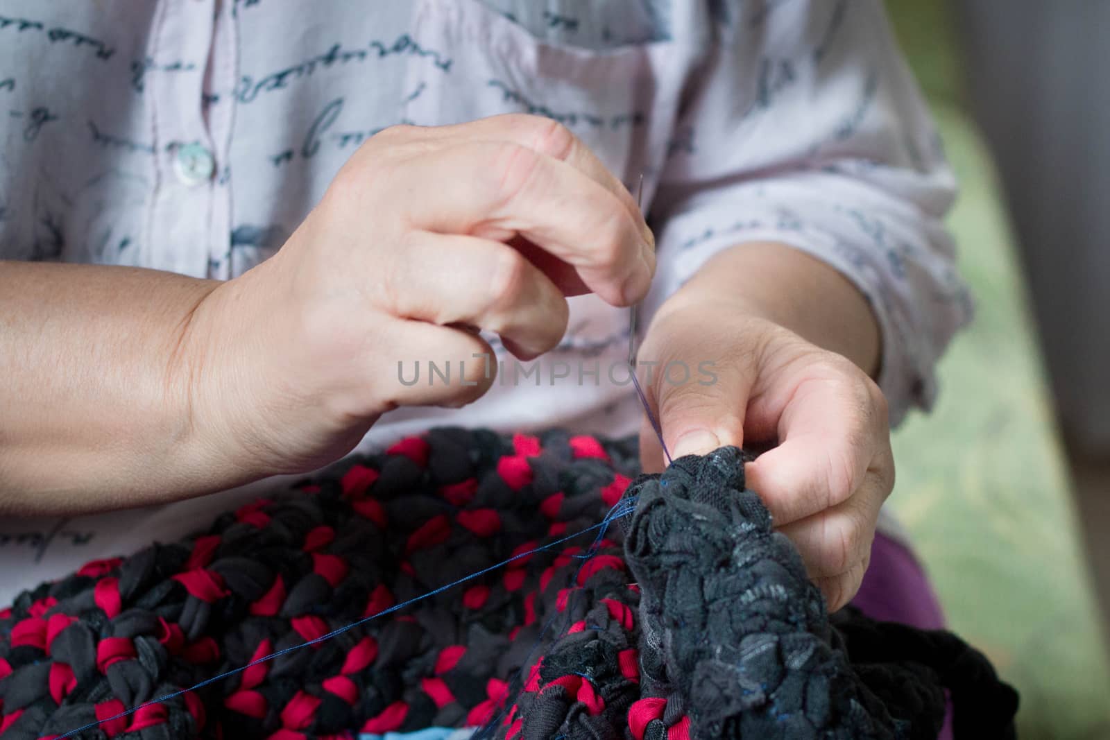 Elderly woman doing hand work sewing with needle and thread by VeraVerano