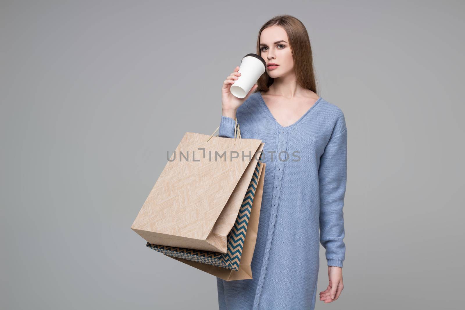 Girl in blue jamper drinking coffee with paper shopping bags by VeraVerano