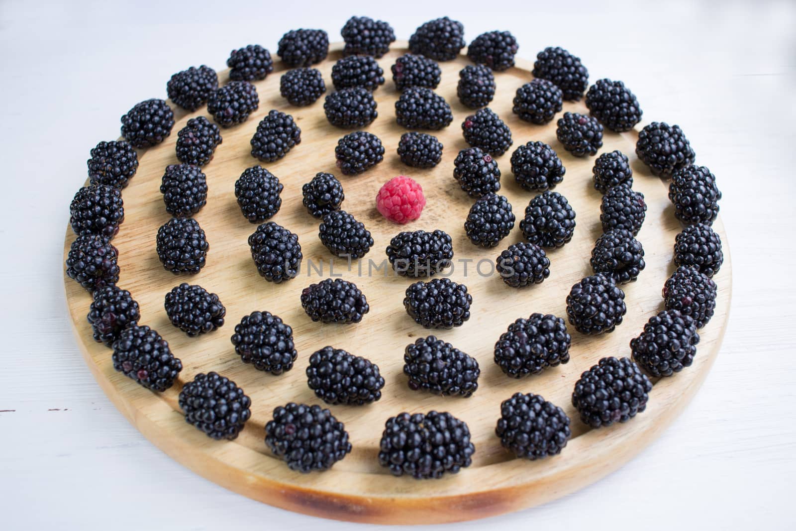 Tasty juicy berries set of many blackberries and one raspberry among them on light round wooden tray isolated