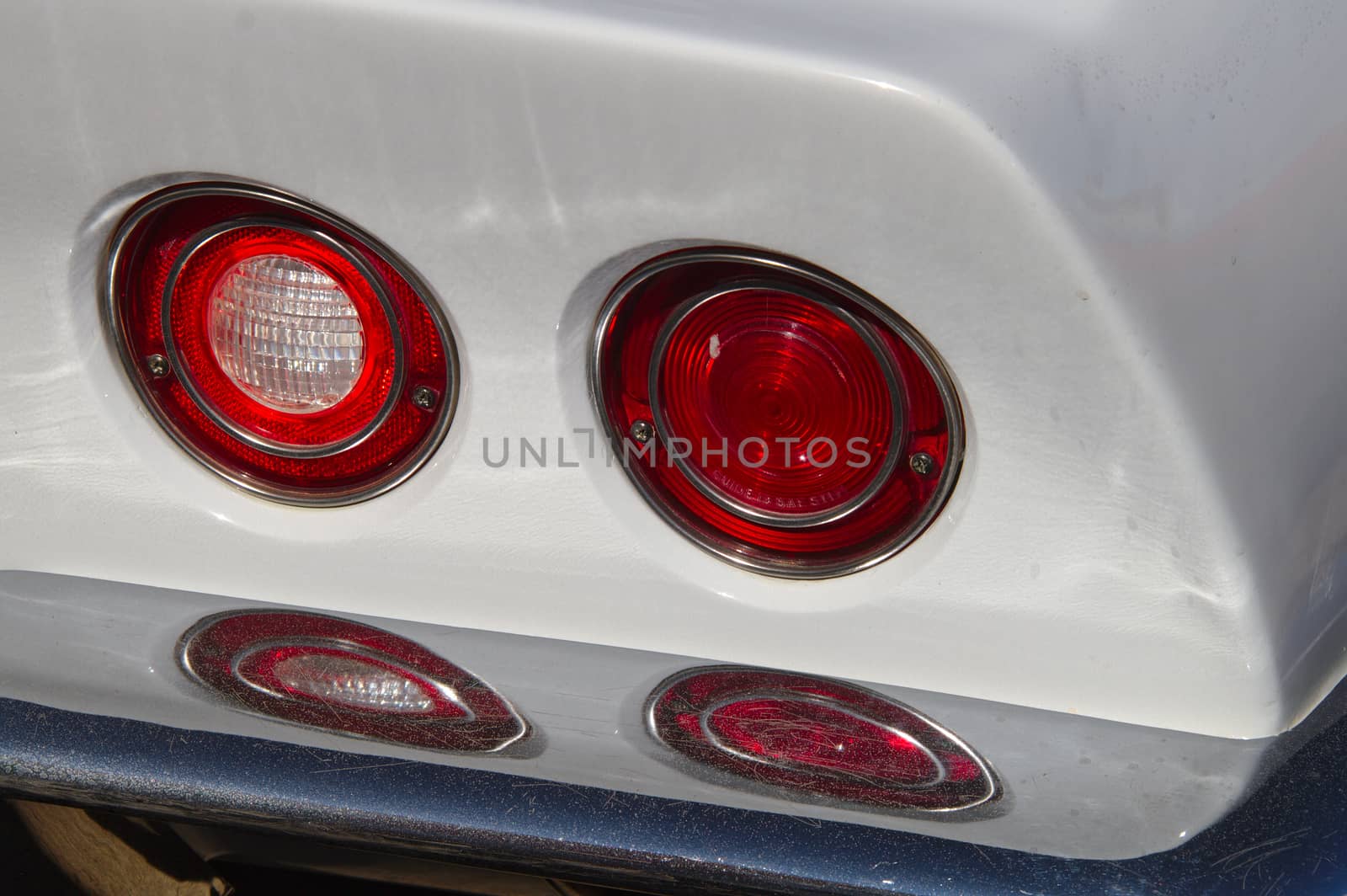 Two round tail light reflecting from chrome rear bumper of a white classic car.