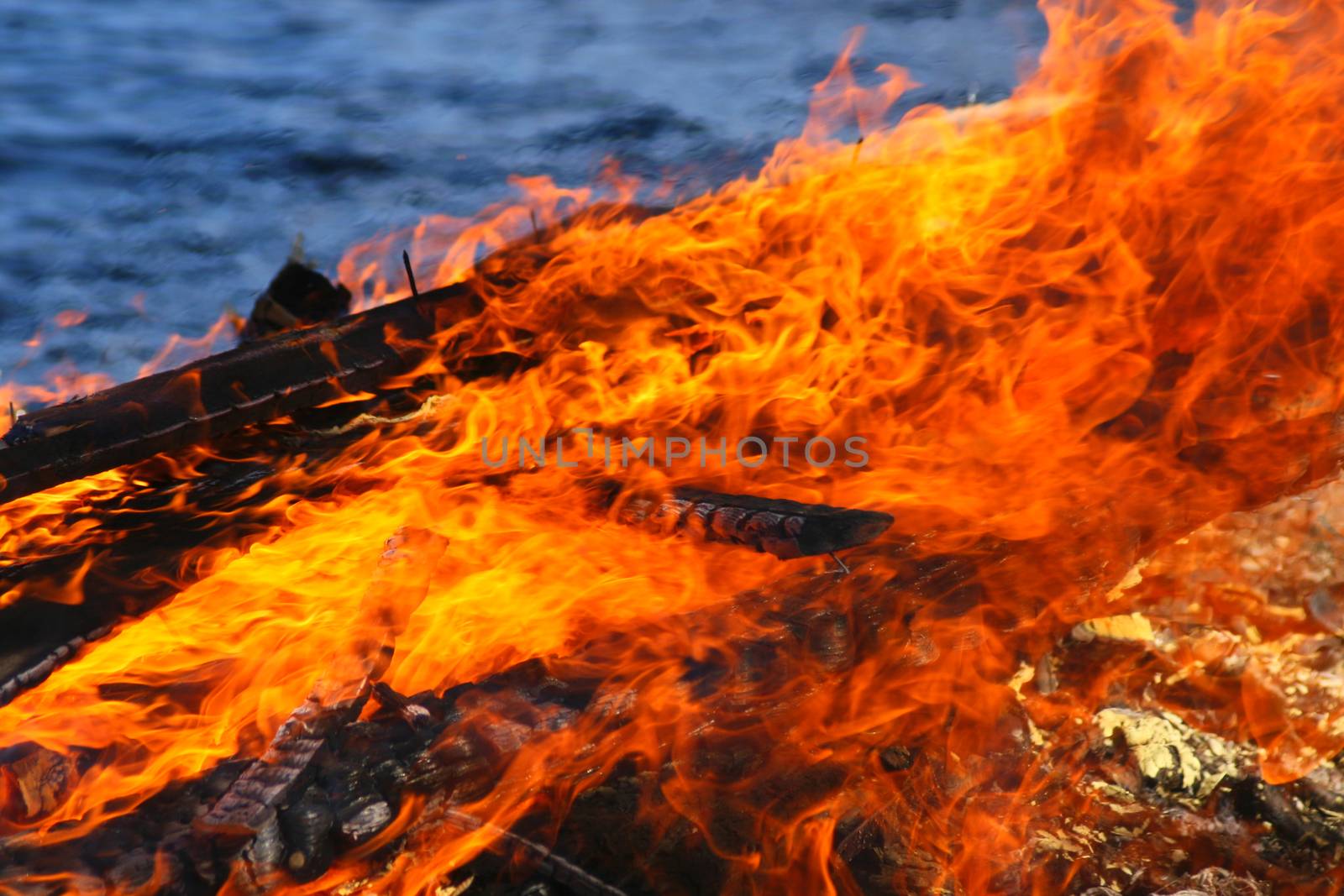 Closeup of a large hot flames burning. Water surface of a lake on blurred background.
