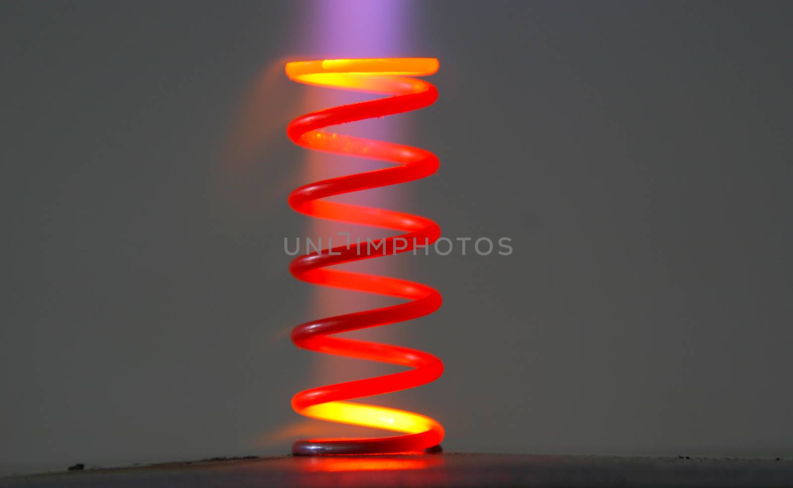 Technical closeup of a steele coil spring heated up to extreme temperatures so metal has changed it's color. Part of the gas flame still visible on the picture with smooth dark background.