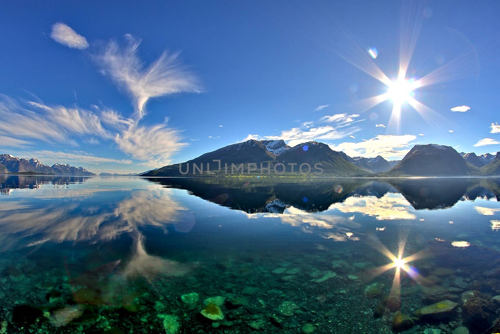 Sun and mountains reflection on the steady surface of Norwegian sea.