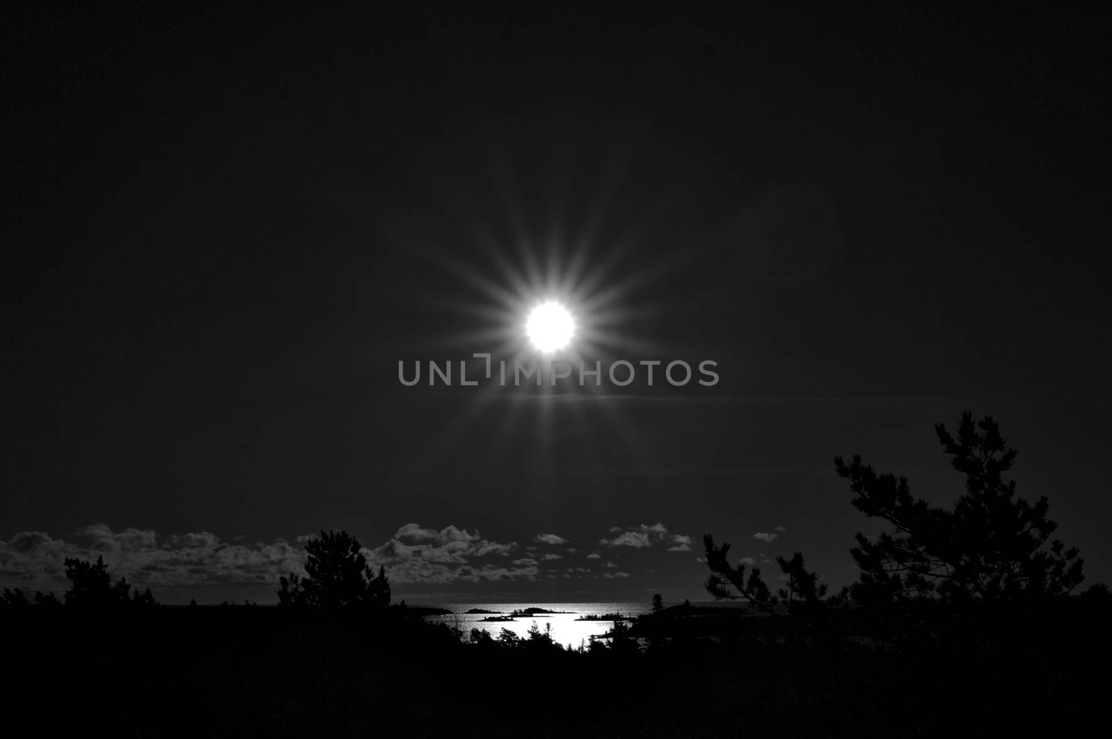 Surreal back and white underexposed photo of the sun shining above the water surface at daytime.