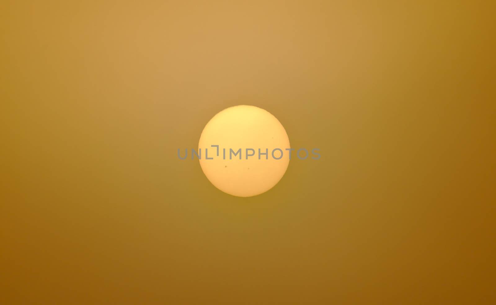 Dark yellow sun shining through misty air. Air pollution has reduced the brightness of the sun so it can be watched even without sunglasses.