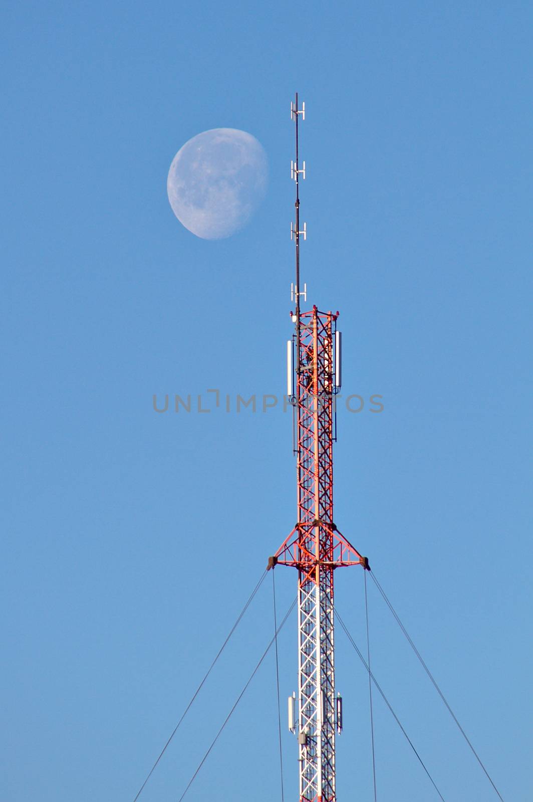 Large moon shining next to top of a telecommunication tower at daytime. Communication to the moon and space. Maybe receiving extraterrestrial signals from other civilizations.