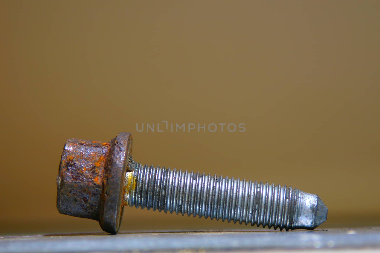Close photo of an old rusty threaded bolt on the table. Light brown blurred background.