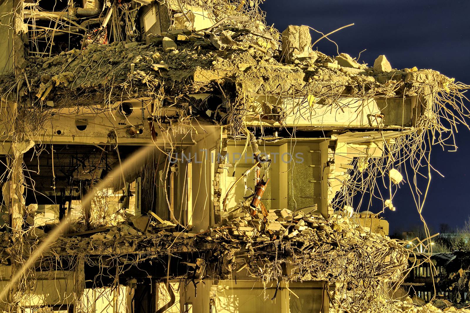 Ruins of an office building with rooms and floors visible through the wall. Cables and pipes hanging, water still flowing from pipes. Dramatic night scene.