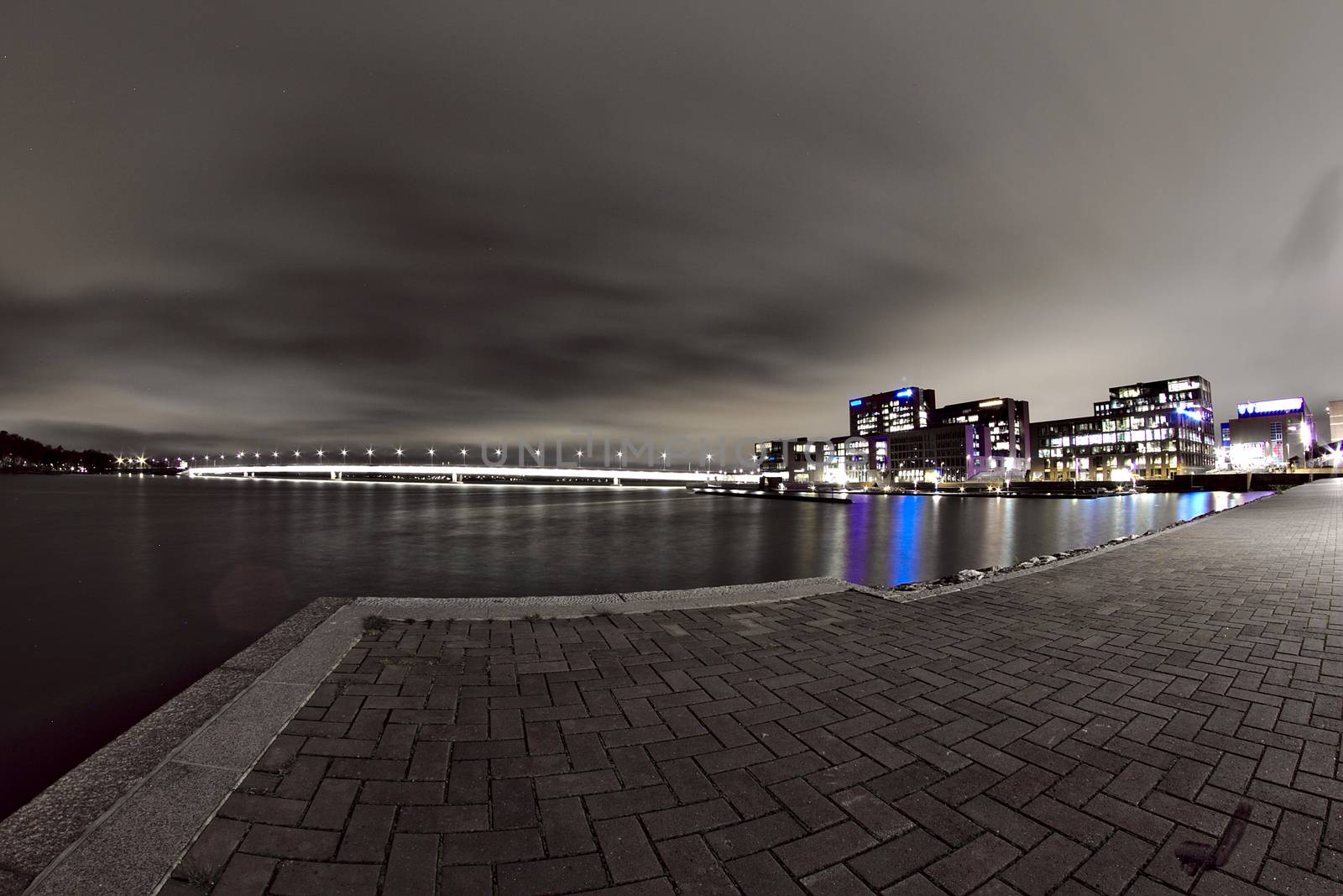 Low angle night photo of Helsinki Salmisaari at night. Long lighted bridge and colorful office buildings on the background of a black and white night photo.