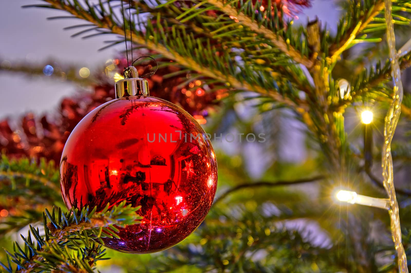 Red round ornament shining on green Christmas tree.