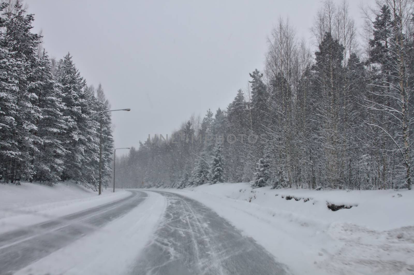 Iced and dangerous roads in the north in wintertime. Snow covering the forest and the road