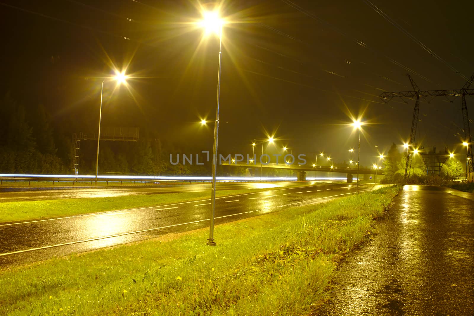 Empty motorway at rainy night with few cars passing leaving light trails.