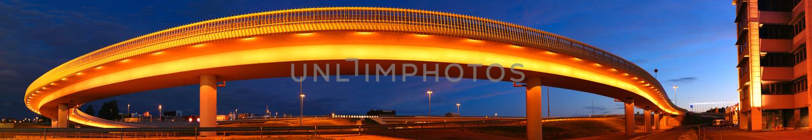 Night photo of a long round lighted bridge. Bridge surrounded with amber lights. Dark blue night sky on the background