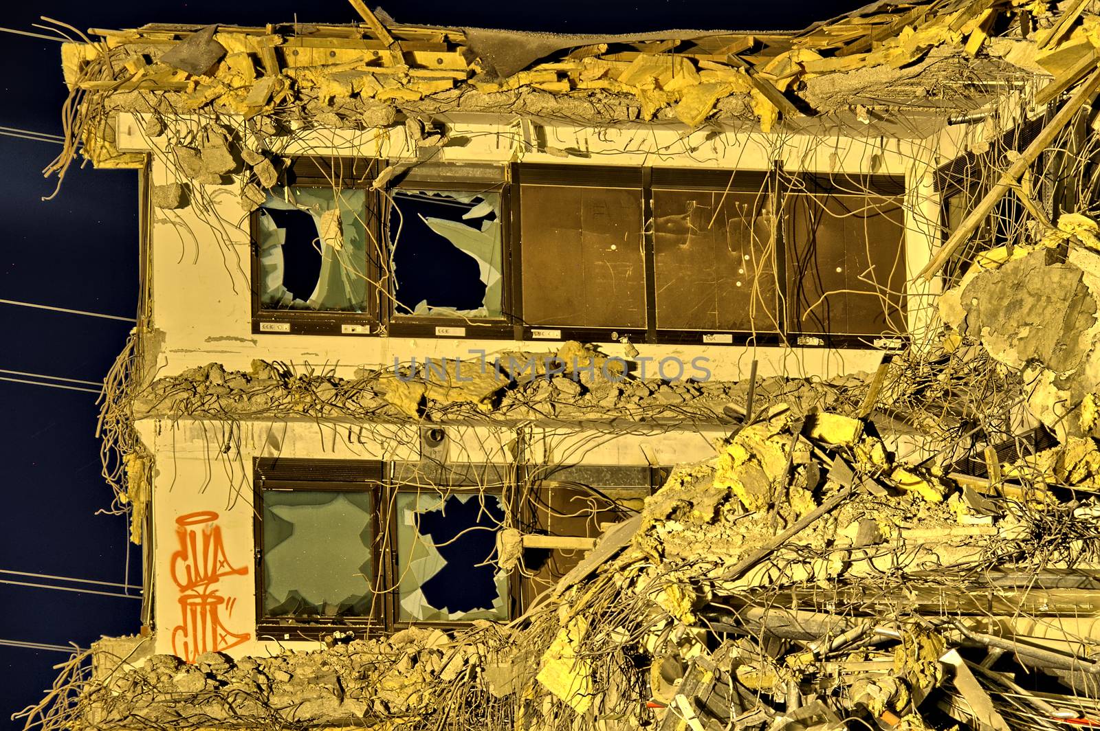 The last wall of an office building still standing with graffiti and broken windows. Some power lines at the background of an apocalyptic photo.