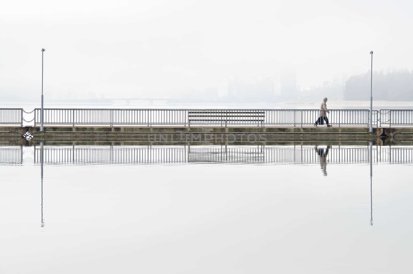 Going to work on a long bridge, early morning in the city. Morning fog still covering the sea and blurring the silhouette of the city on the background. Clear reflection from steady water surface.