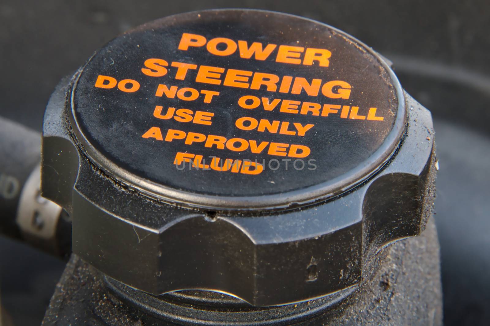 Closeup of a cap of a power steering oil tank. Do not overfill and use approved fluid only warning text.
