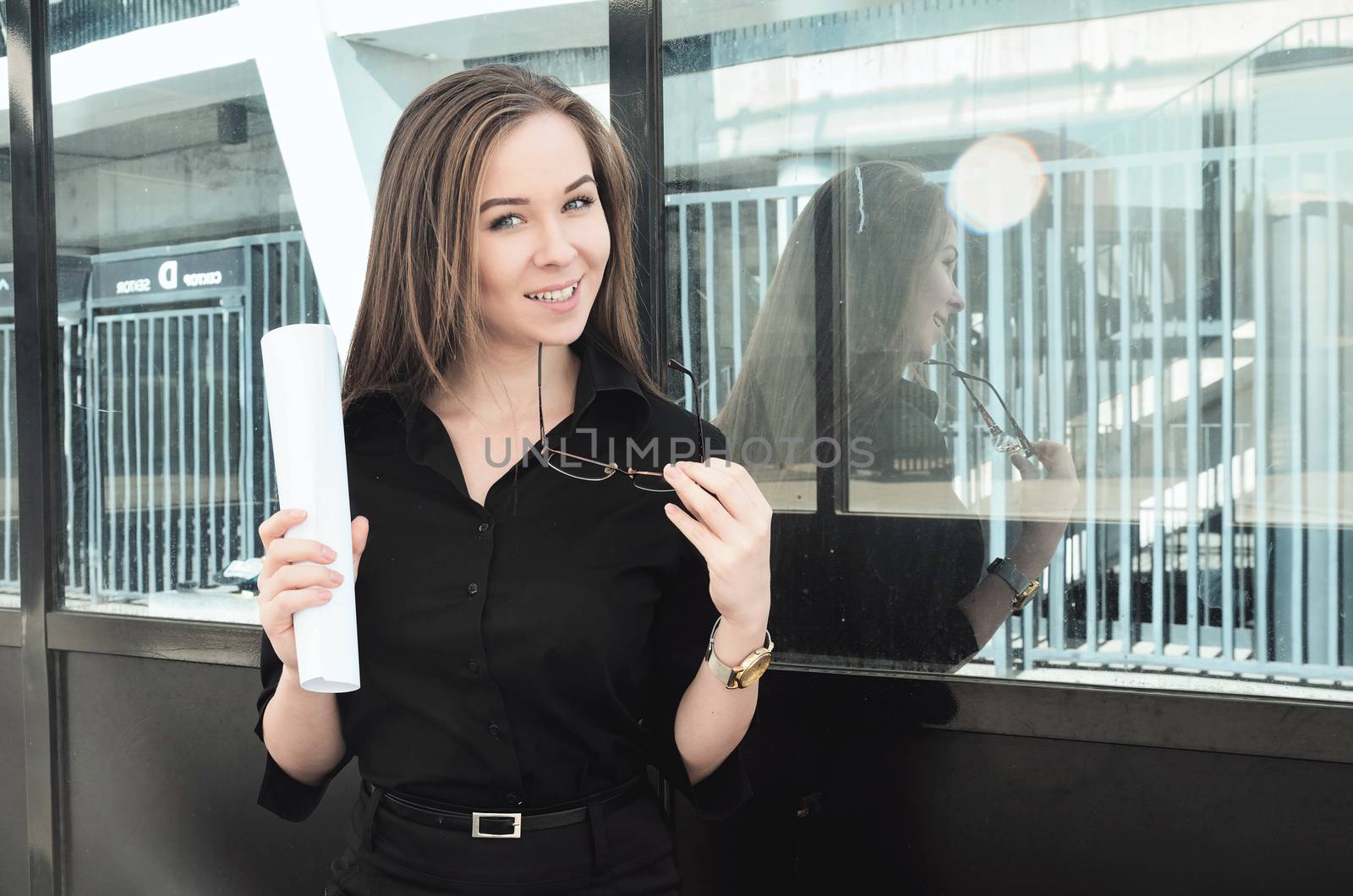beautiful young girl engineer holding a sheet of paper and glasses, happy to complete the project, standing near the building in the open area