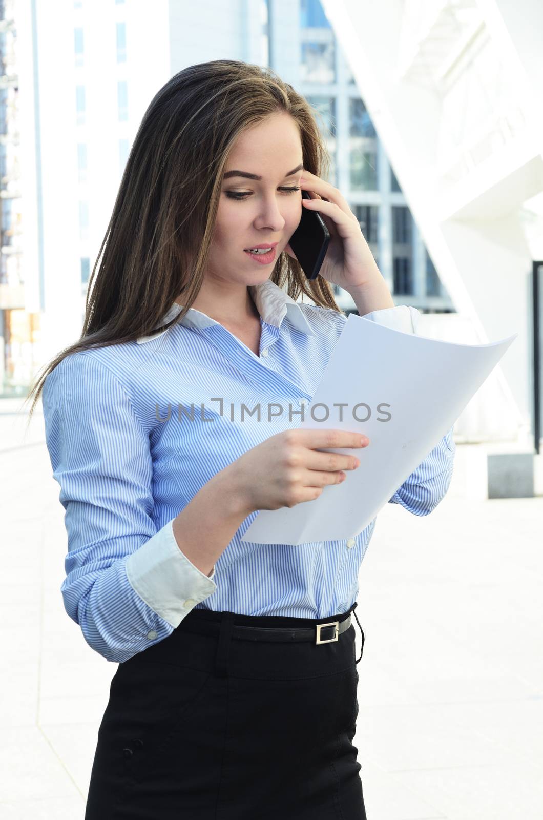 Young beautiful and successful business lady solves questions on the phone reading information from a sheet of paper