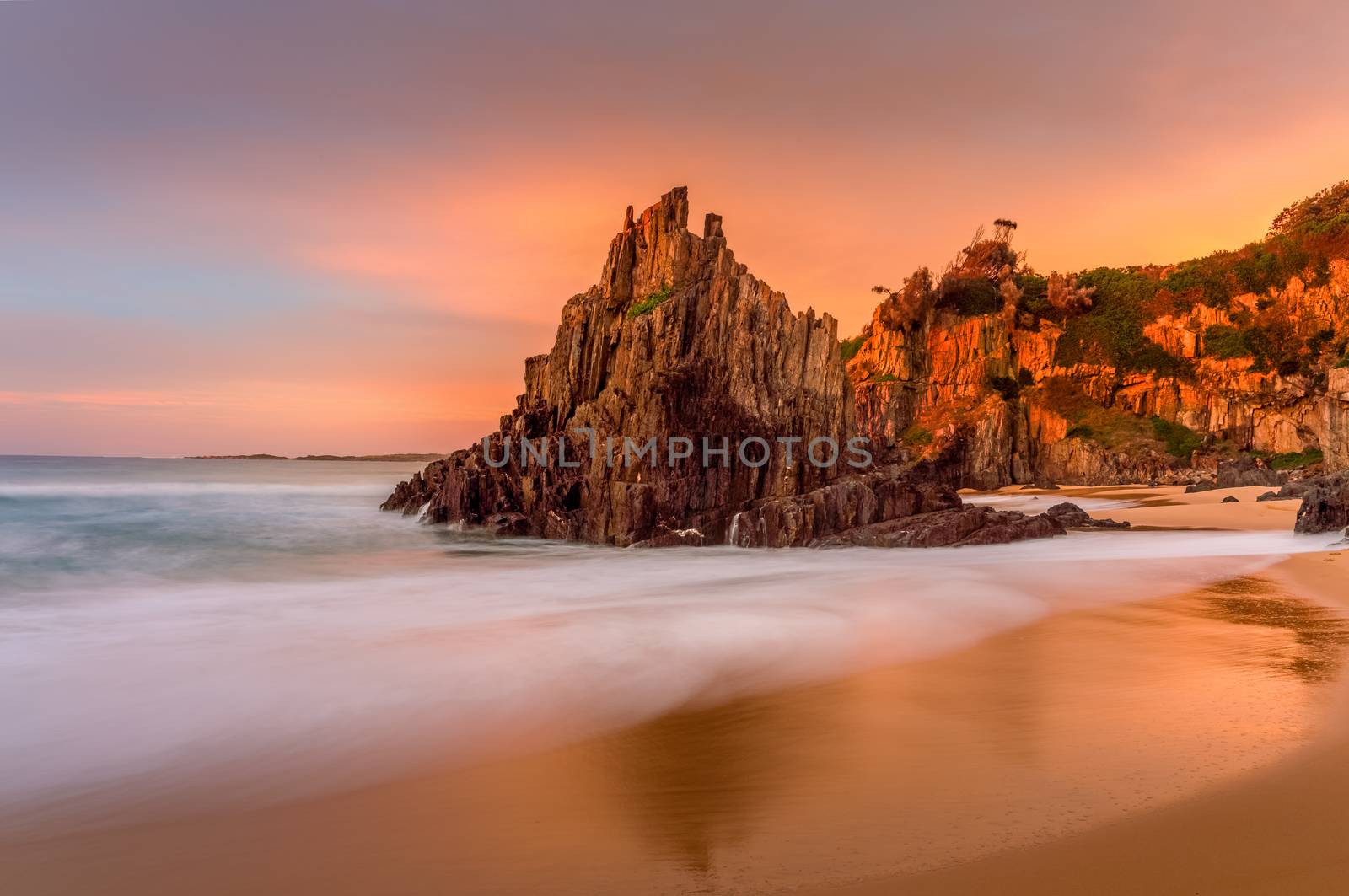 Beautiful sunrise light at Bingie Beach with soft motion flows around the pyramid rock sea stack