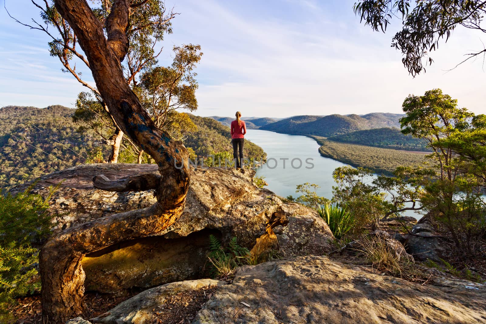 Female standis on the edge of the cliff with clear views out over the snaking river and mountain scenery