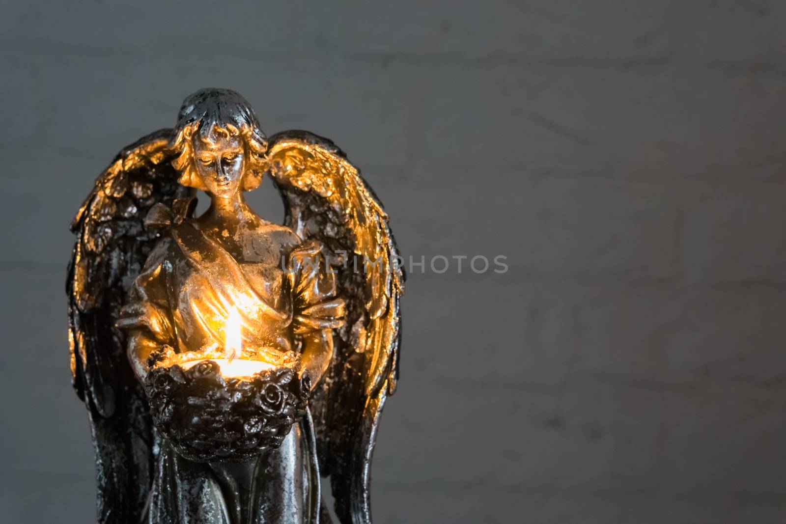 closeup of a silver angel statue holding a lighted candle, christmas and spiritual tradition by charlottebleijenberg