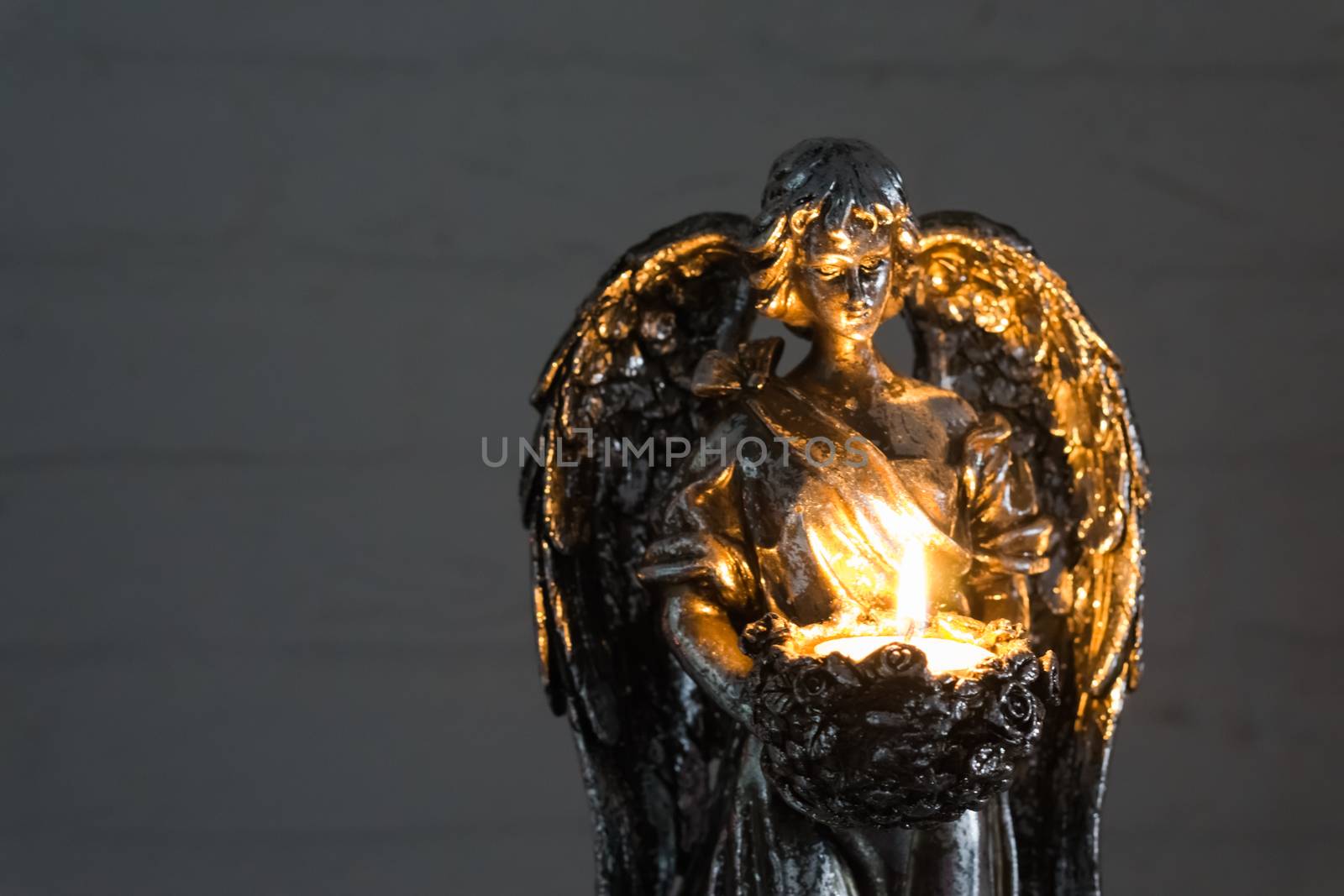 silver angel statue holding a burning candle in closeup, christmas and spiritual tradition