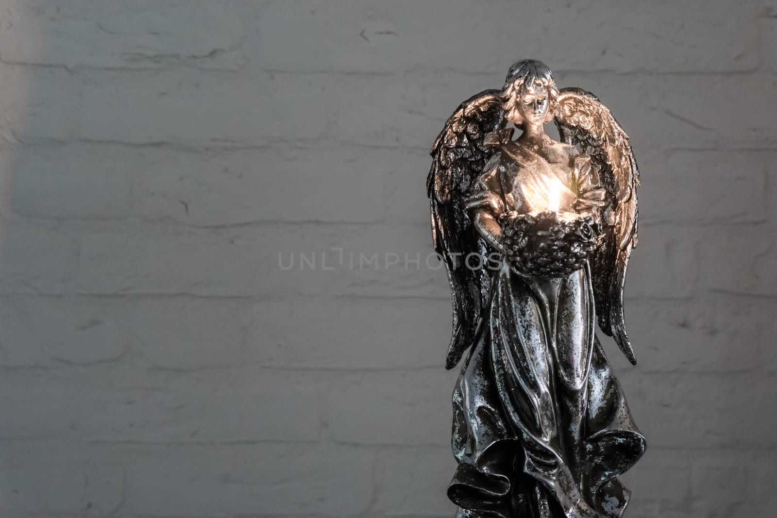A silver angel statue holding a burning tea light candle, Traditional christmas or spiritual background by charlottebleijenberg