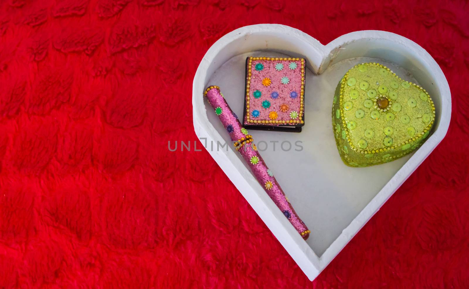 Valentines day decorations background, a white heart shaped box with a pen, note book and heart shaped box laying on a red pillow by charlottebleijenberg