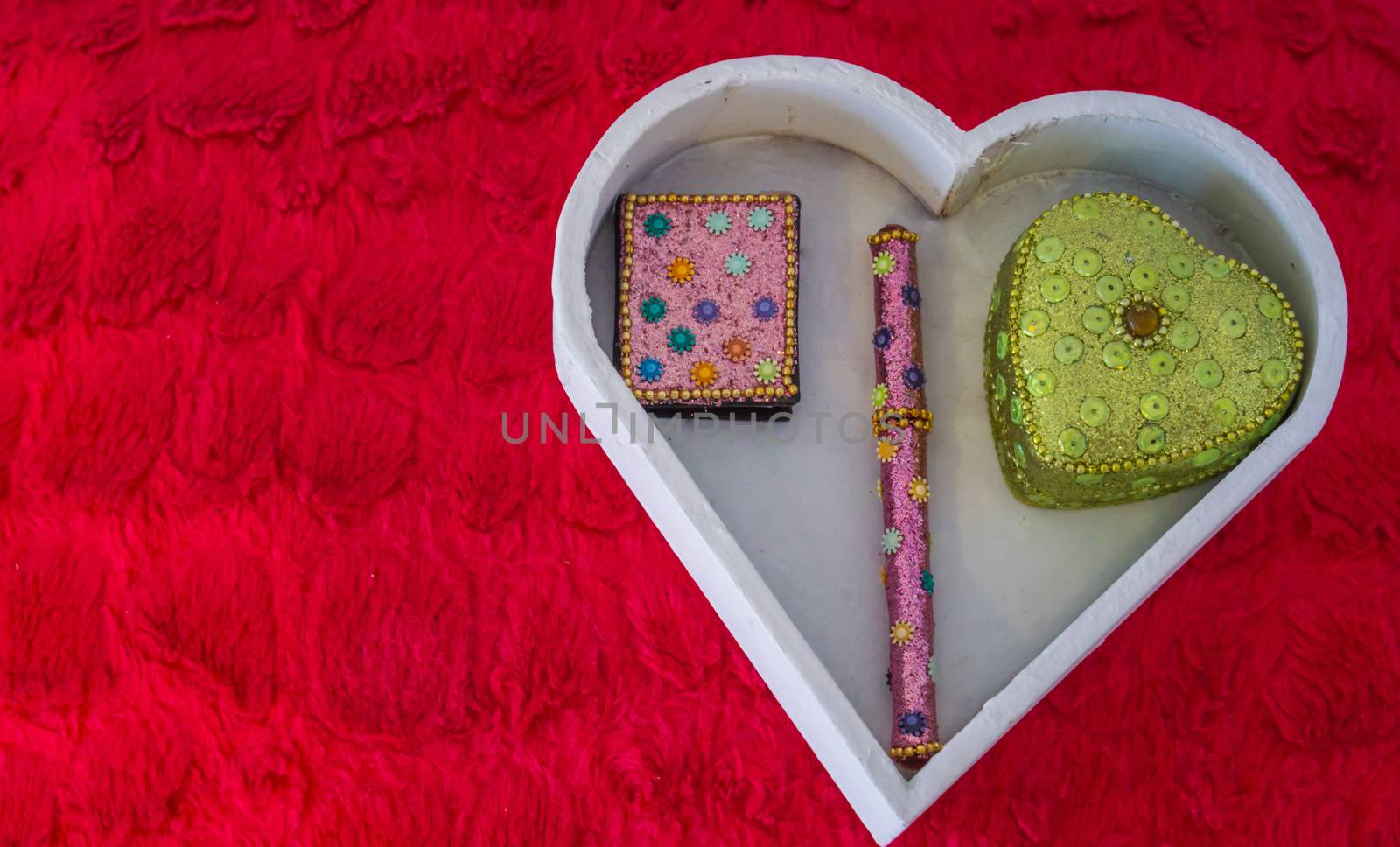 valentines day decorative background, a white heart shaped box with a notebook,pen and heart shaped box in it laying on a red pillow