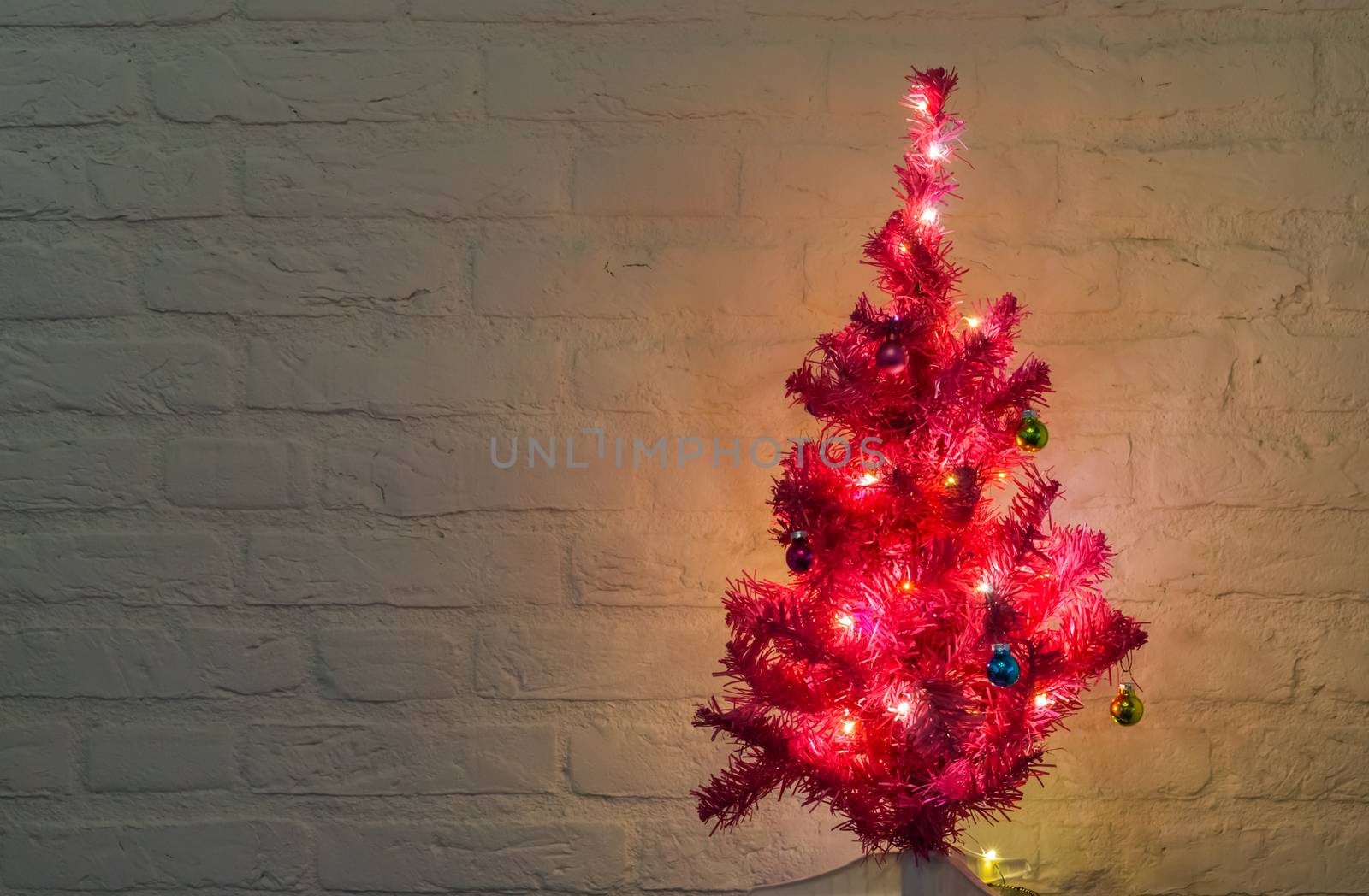 lighted and decorated christmas tree isolated on a white brick wall background