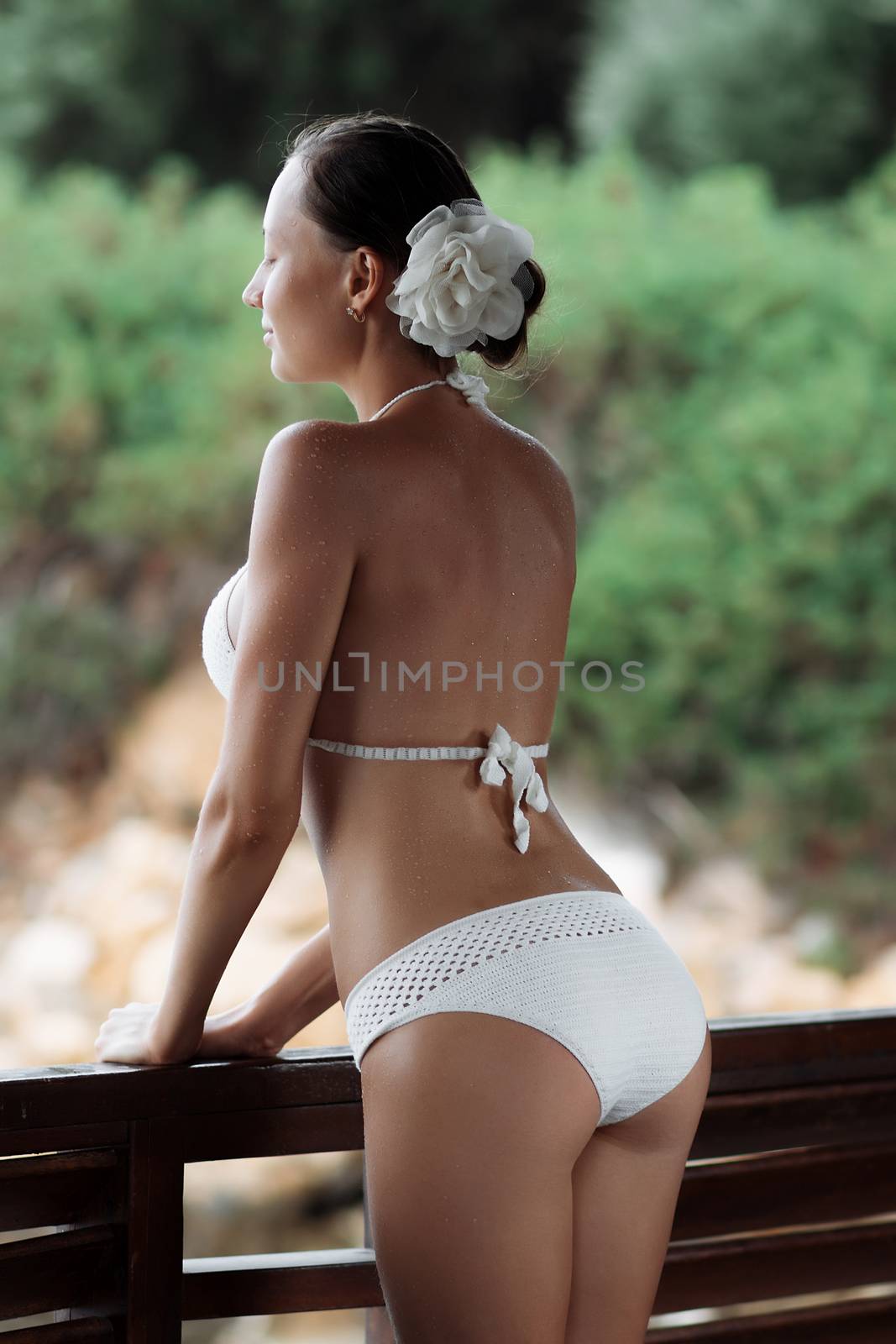 Sensual young lady in knitted swimwear embracing herself and keeping eyes closed while standing near amazing calm sea