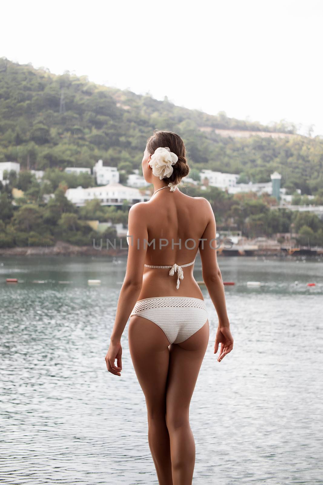 Sensual young lady in knitted swimwear embracing herself and keeping eyes closed while standing near amazing calm sea