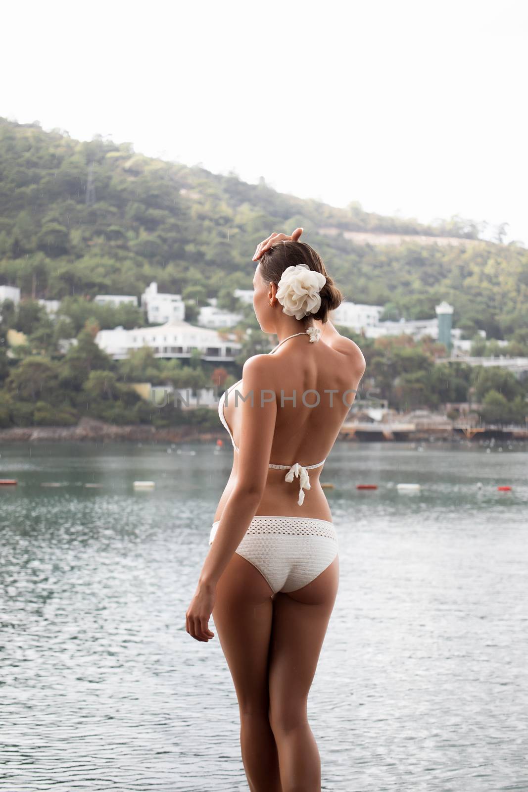 Sensual young lady in knitted swimwear embracing herself and keeping eyes closed while standing near amazing calm sea