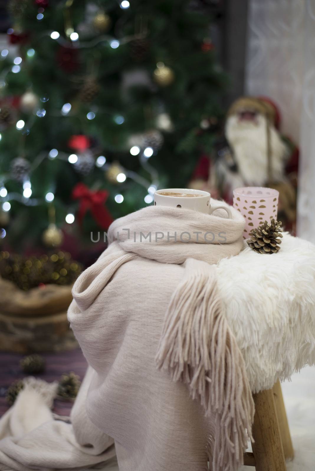 Christmas time. Hot chocolate, a cup of cappuccino on a fur chair in front of a large Christmas tree with balls and lights. Warm scarf, cones around