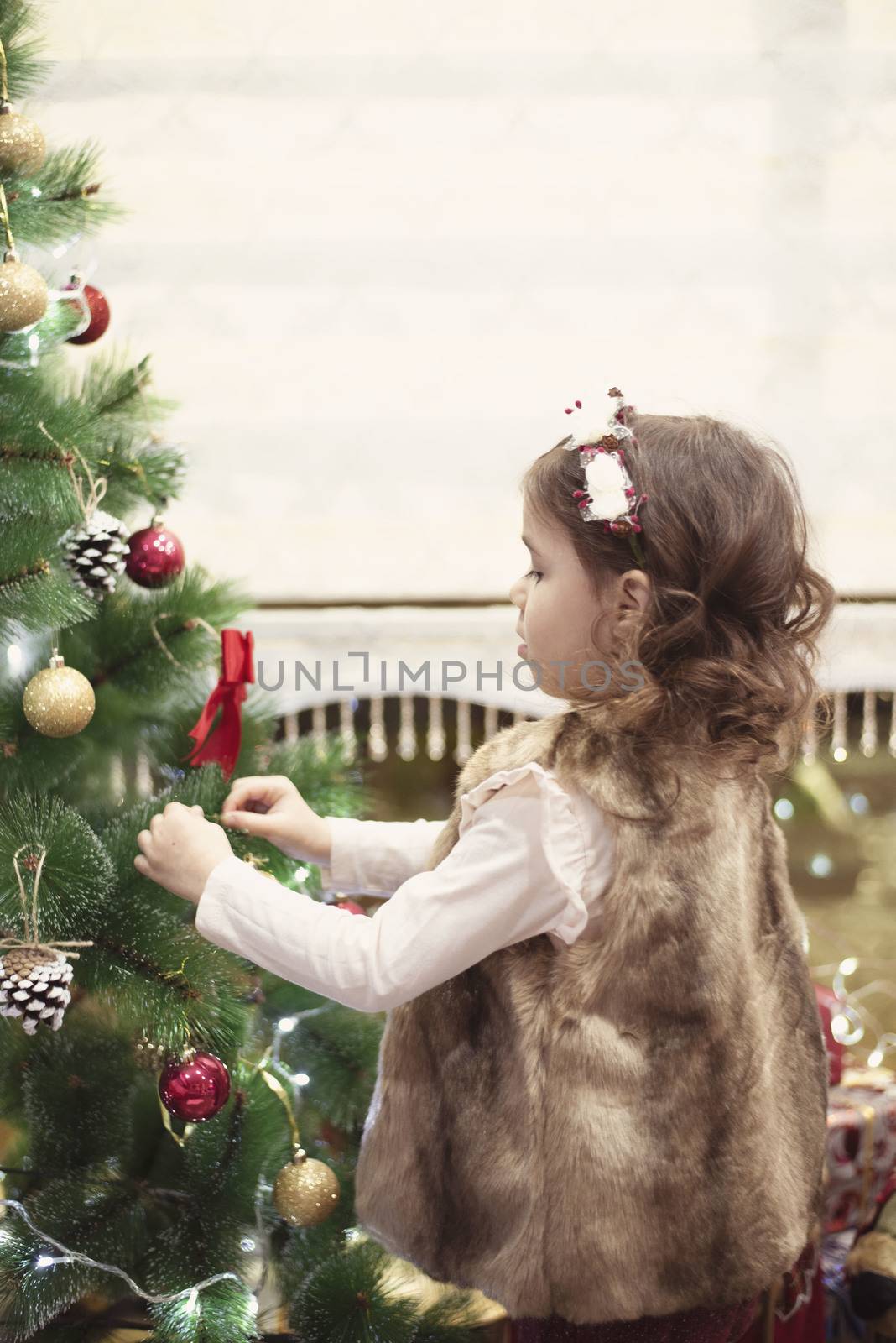 Little child girl decorating Christmas tree with balls at home, indoors. Close up. Christmas concept by sevda_stancheva