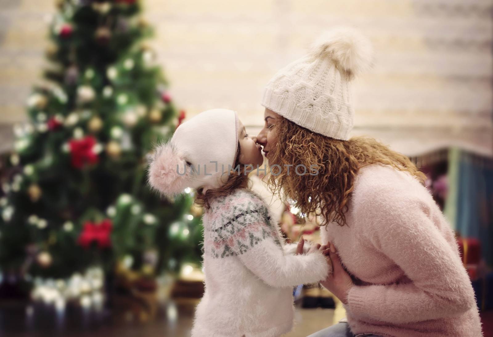 Happy Christmas and Happy Holidays concept. Cheerful mom and her cute daughter having fun in cozy decorated living room near the Christmas tree. Mother is kissing, hugging the little girl by sevda_stancheva