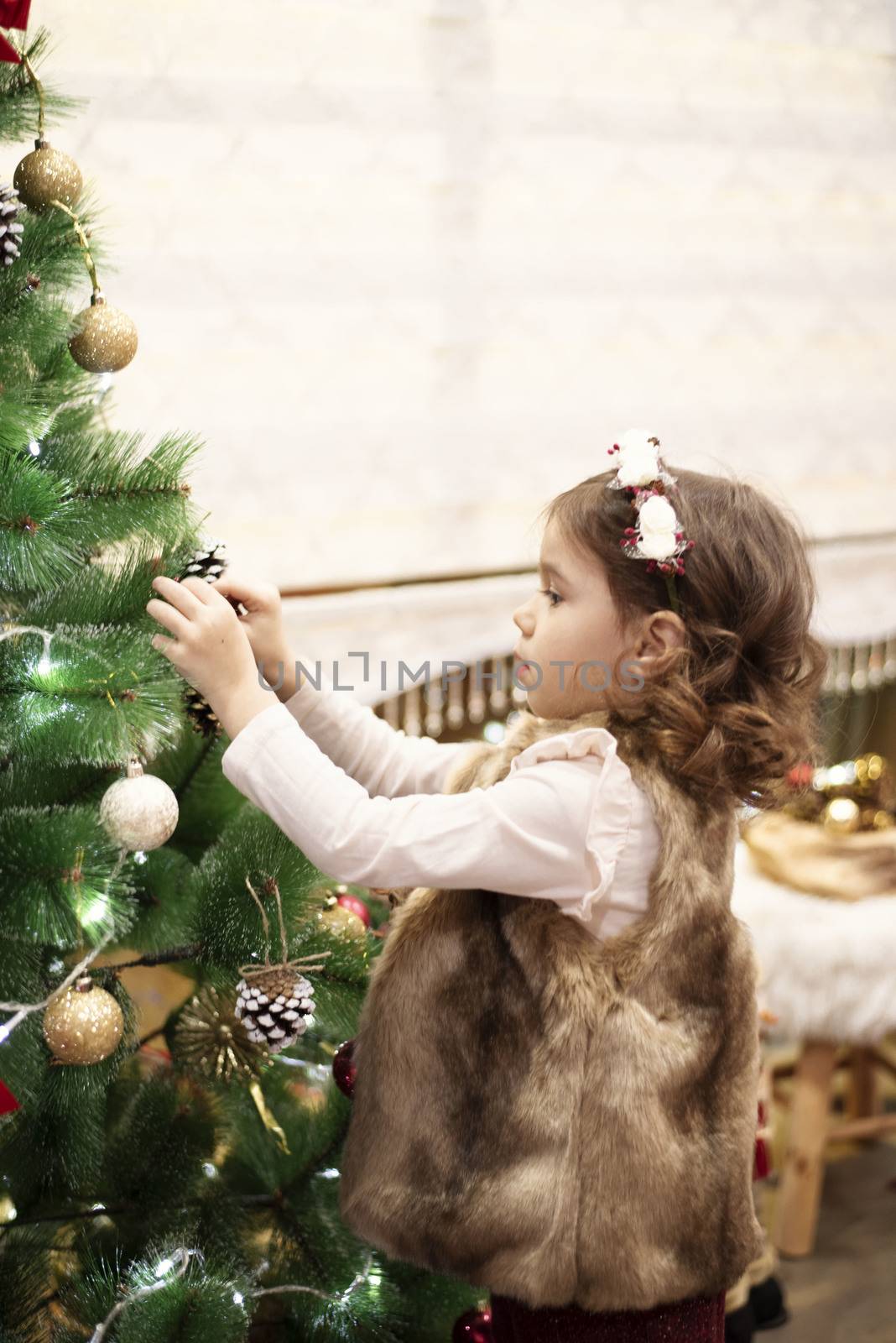 Little child girl decorating Christmas tree with balls at home, indoors. Close up. Christmas concept.