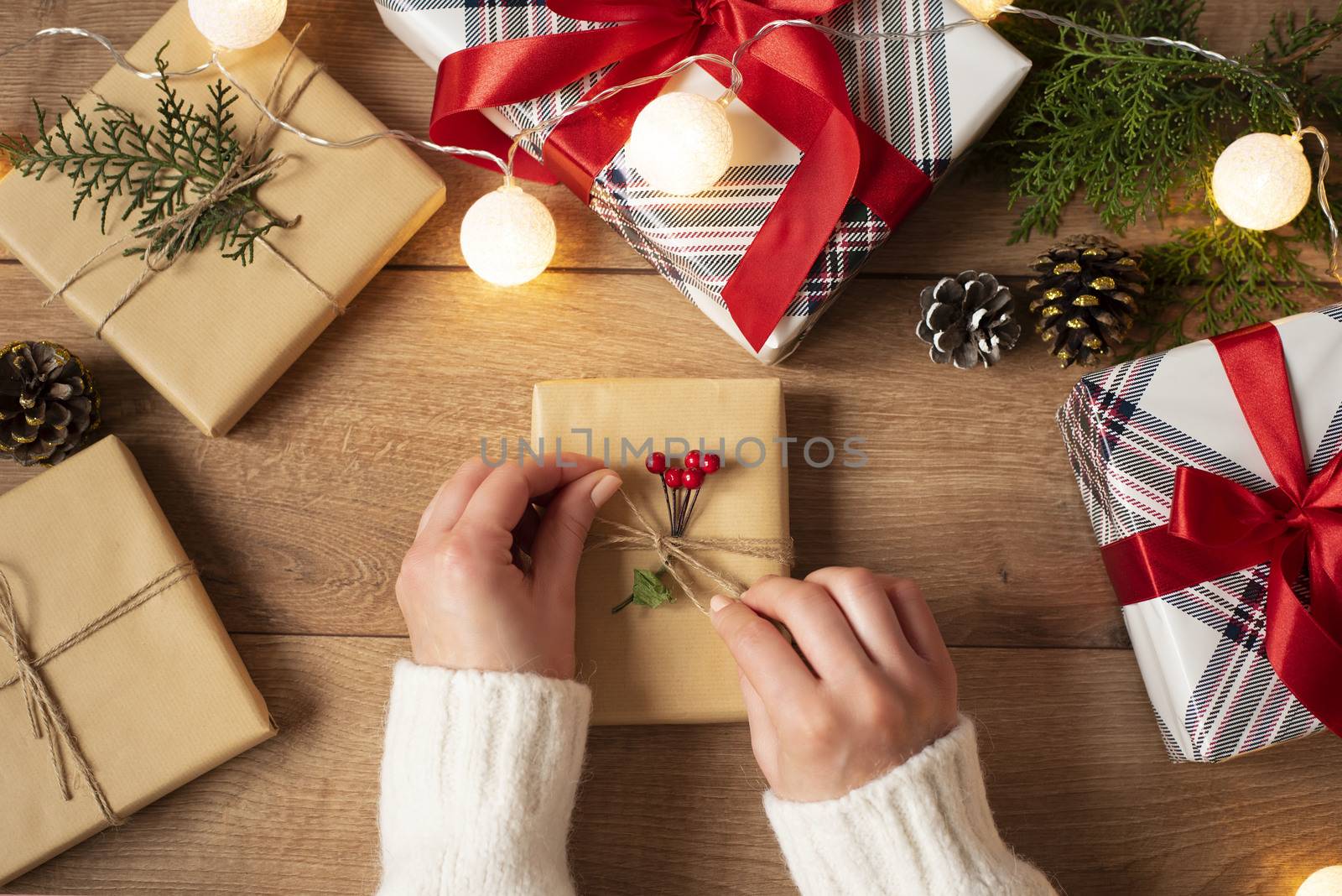 Woman's hands tying the bow on vintage present on rustic background. Festive backdrop for winter holidays: Birthday, Valentines day, Christmas, New Year. Flat lay of woman packing gift boxes.