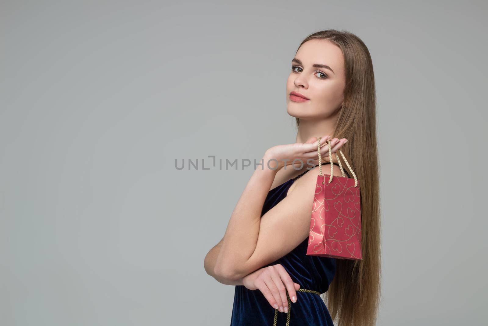 Young model long-haired blond girl in dark blue dress holds red paper gift present package