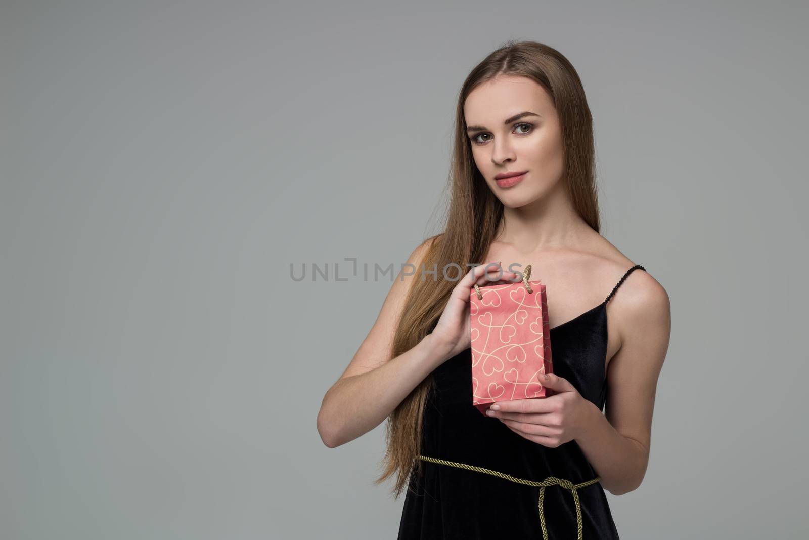 Young model long-haired blond girl in black holds red paper gift present package