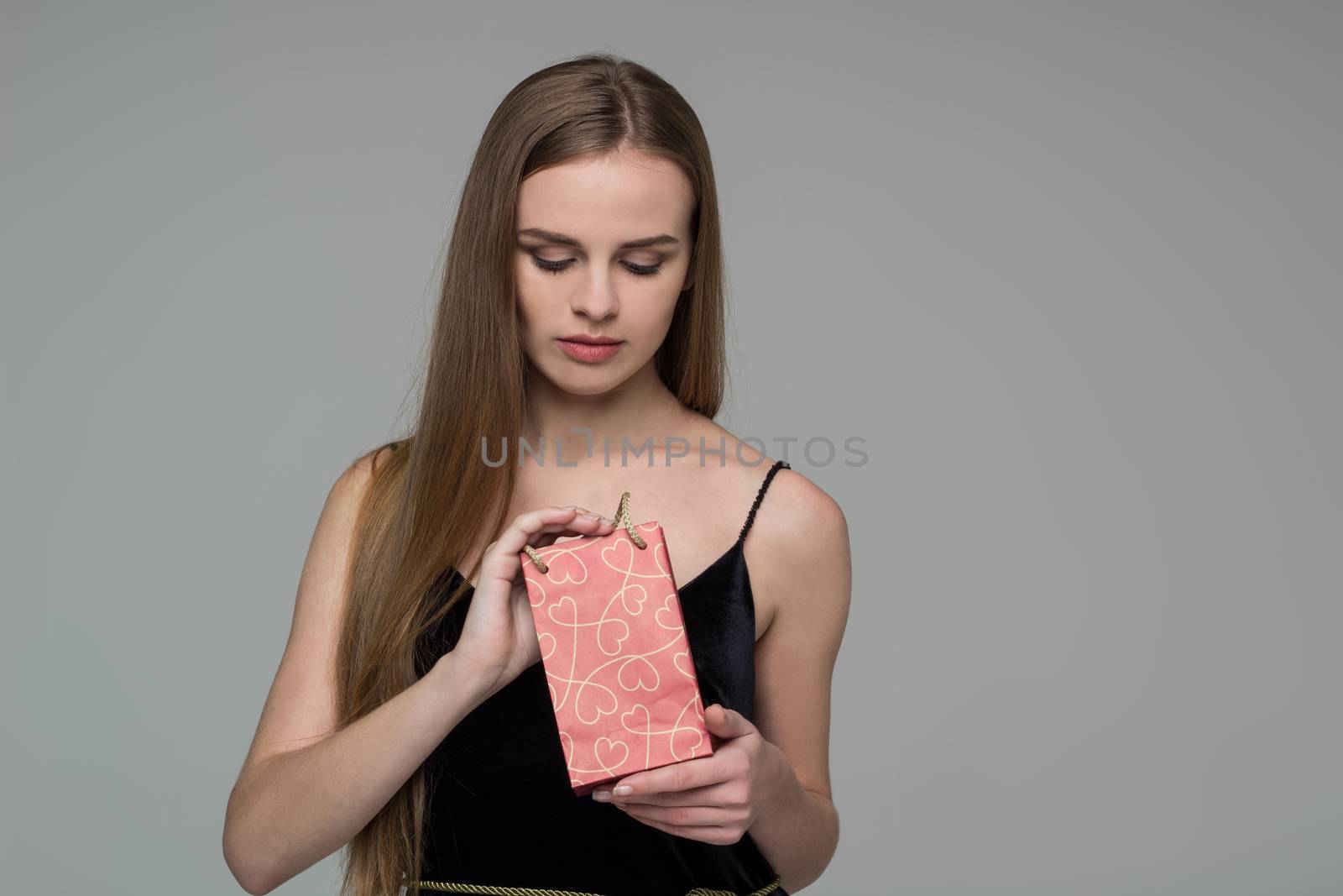 Young model long-haired blond girl in black holds red paper gift present package
