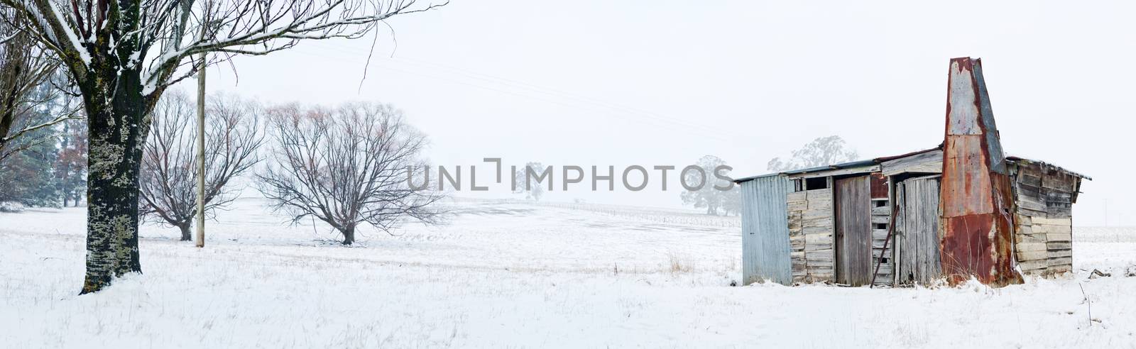 Rustic timber cabin or shed made from mismatched timbers, rusted metal and corrugated iron sits in a snow covered rural field in winter