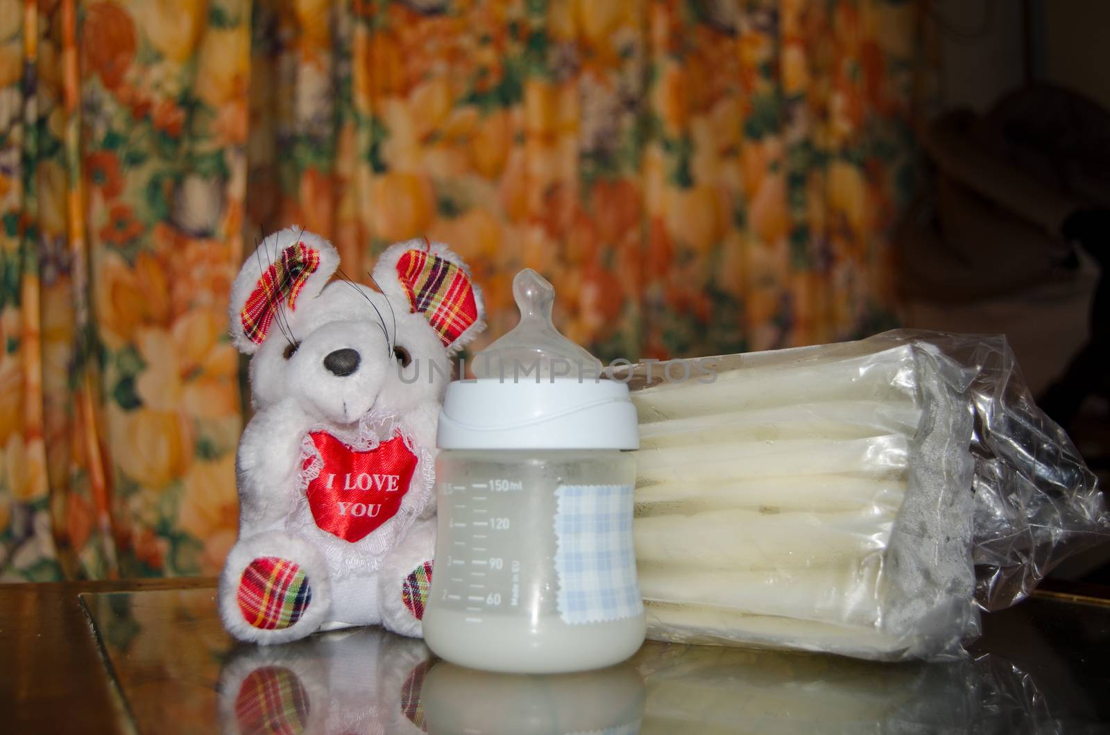 baby bottle with fresh expresed milk, frozen breastmilk in storage bags and soft toy mouse, breasfeeding concept