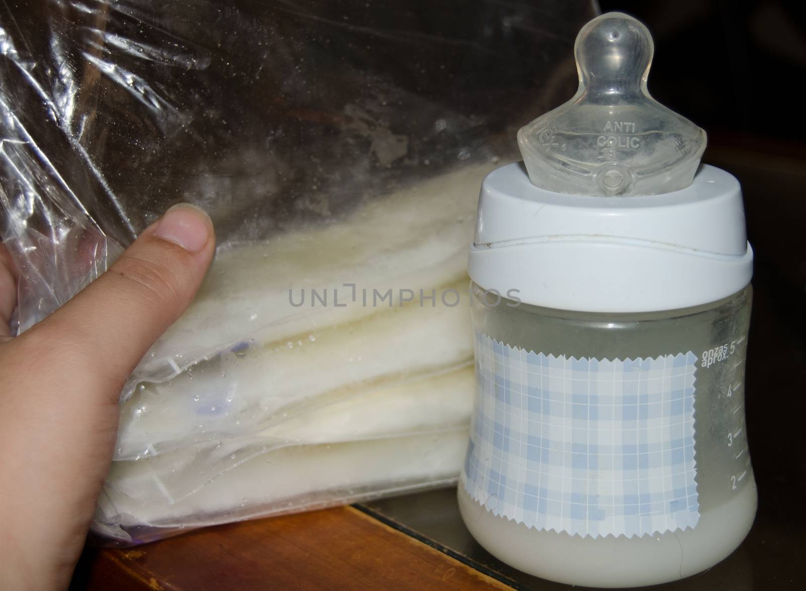 woman hand holding frozen breast milk in storage bags and baby bottle with fresh expresed breastmilk, breastfeeding concept